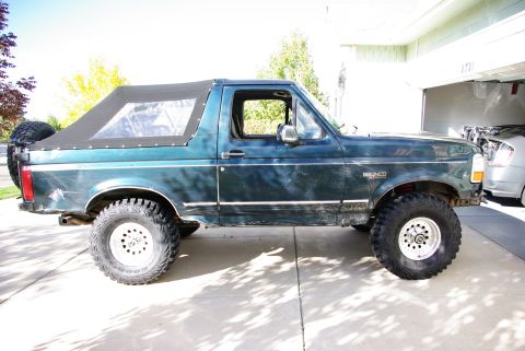 1995 Ford Bronco - A green Ford Bronco with a soft top is parked in a driveway next to a garage.