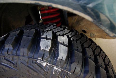 1995 Ford Bronco - A close-up view of a tire and its red coilover suspension system, with "SUPERMOTORS" text visible at the bottom right.