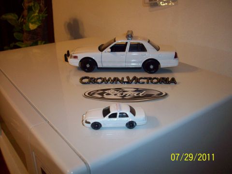 1998 Ford Crown Victoria - Toy models of police cars and their corresponding emblems are displayed on a flat surface.