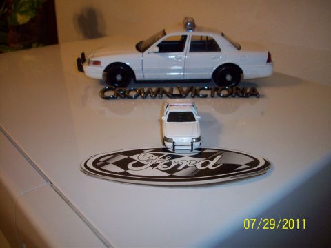 1998 Ford Crown Victoria - Two toy cars are displayed on a surface with a Ford emblem and the text 'CROWN VICTORIA'.