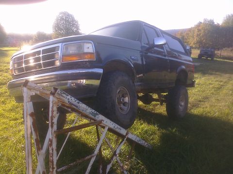 1995 Ford Bronco - A dark-colored Ford Bronco is positioned on a metal ramp in a grassy field with another vehicle visible in the distance.
