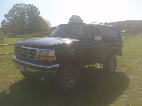 1995 Ford Bronco - This black Ford Bronco is viewed from the front three-quarter angle, parked in a grassy field.