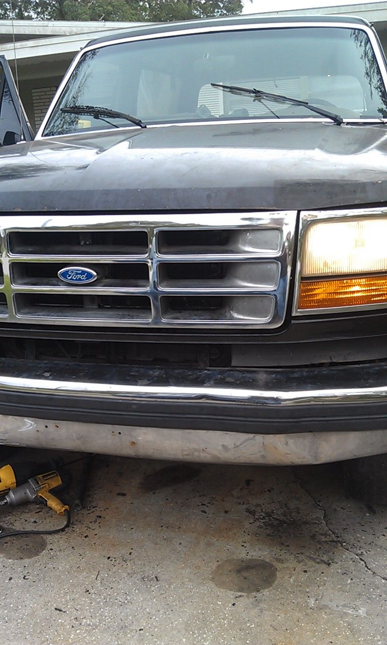 Front view of black Ford Bronco with chrome grille, headlight on, DeWalt impact wrench on driveway below bumper