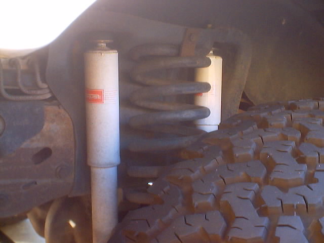 Underbody view of front coil spring, shock absorber and mud-terrain tire tread under a truck