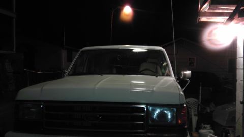1989 Ford Bronco - A white Ford Bronco is parked outside at night, with its headlights illuminated.