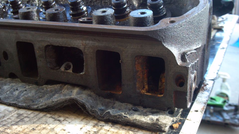 Dirty cast-iron cylinder head on a workbench showing rusty ports and valve springs