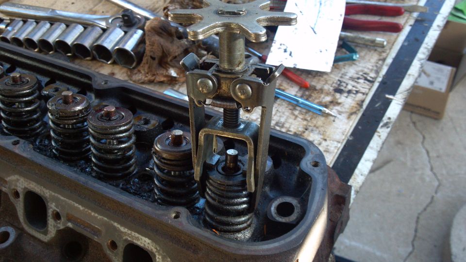 Valve spring compressor tool on a cylinder head with springs exposed, tools on workbench behind