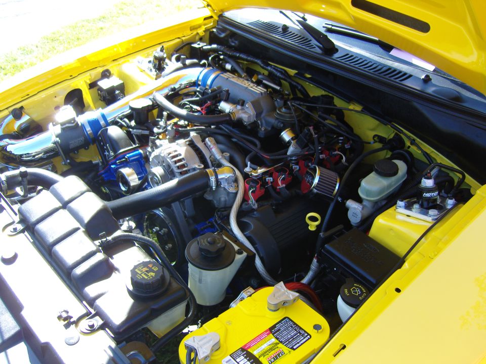 Yellow 2007 Ford Mustang engine bay with blue intake piping and yellow battery