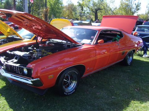 2007 Ford Mustang - A vintage orange muscle car is displayed with its hood open at a car show, its engine bay.