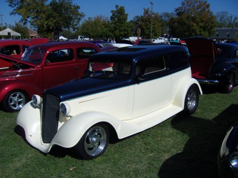 2007 Ford Mustang - A vintage two-tone sedan hot rod is displayed at an outdoor car show with other vehicles.