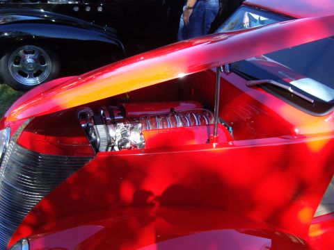 2007 Ford Mustang - A red hot rod displays its polished V8 engine under an open hood, with another vehicle in the background.