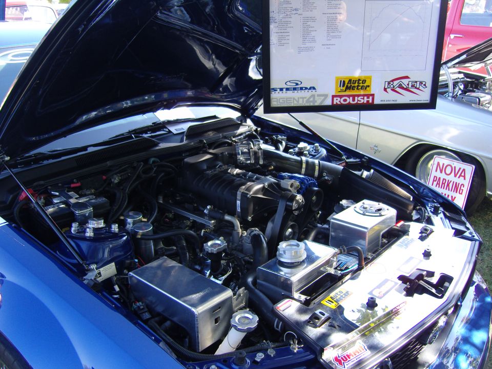 Blue engine bay with supercharger, intercooler, and various aftermarket parts. A sign for 'Nova Parking Only' is visible