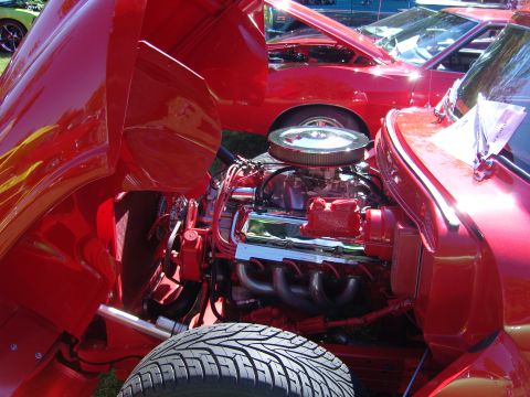 2007 Ford Mustang - A bright red engine bay is visible with the hood open, chrome accents and a tire in the foreground. Another red car is partially visible be…