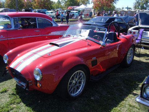 2007 Ford Mustang - A red convertible sports car with racing stripes is parked on the grass at an outdoor car show.