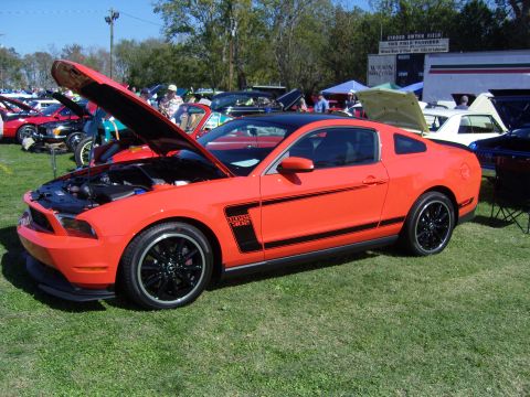 2007 Ford Mustang - A bright orange Ford Mustang Boss 302 is displayed with its hood open at an outdoor car show.