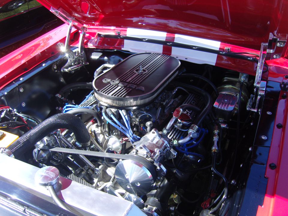 Red 1967 Ford Mustang engine bay with a Cobra air cleaner and dual racing stripes on the hood