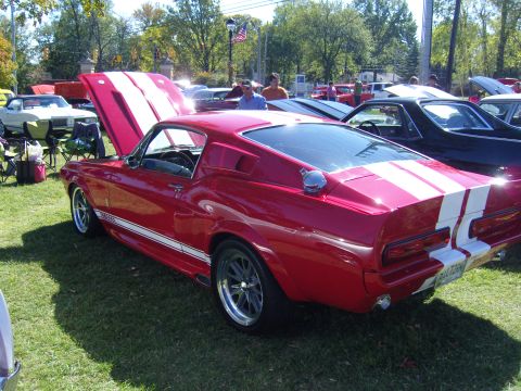 2007 Ford Mustang - Classic red 1967 Ford Mustang Shelby GT500 with racing stripes at a car show.