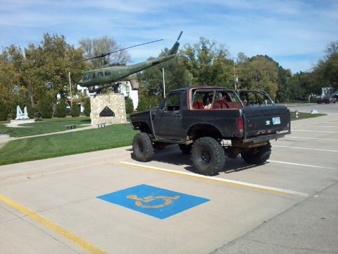 1986 Ford Bronco - A lifted black Ford Bronco is parked in a handicapped spot, with a helicopter monument in the background.