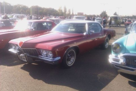 1991 Ford LTD Crown Victoria - A classic red Buick Riviera is displayed at an outdoor car event, surrounded by other vintage automobiles.