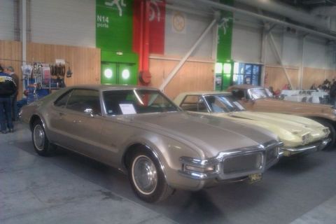 1991 Ford LTD Crown Victoria - A gold 1966 Oldsmobile Toronado is displayed indoors next to other classic cars.