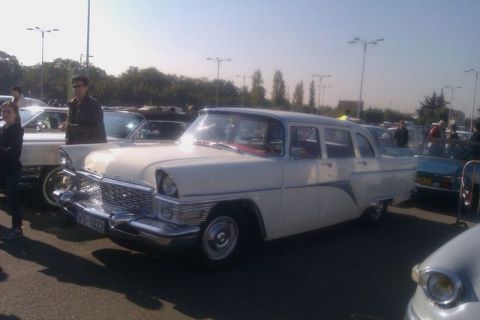1991 Ford LTD Crown Victoria - A white sedan with extensive chrome trim is parked outdoors with other vehicles and people.