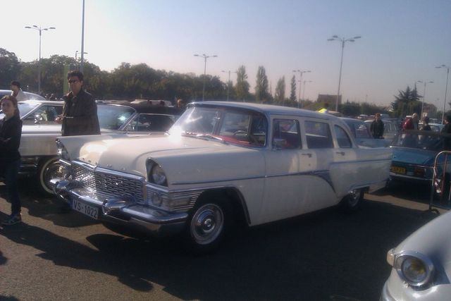 White sedan with chrome grille and trim, license plate VS-1022. Other cars and people visible