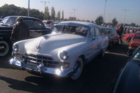 1991 Ford LTD Crown Victoria - A classic white Cadillac sedan is parked at an outdoor event with other vehicles around.