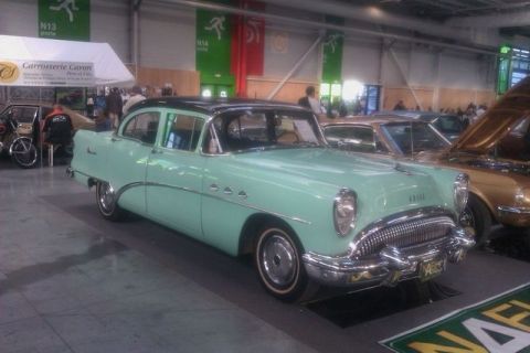 1991 Ford LTD Crown Victoria - A mint green 1955 Buick sedan with a black roof is displayed indoors, alongside other vehicles.