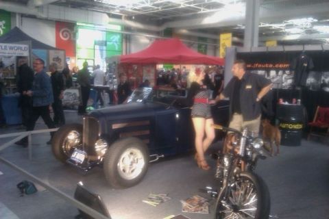 1991 Ford LTD Crown Victoria - A hot rod car and a motorcycle are displayed indoors, with people milling around in the background.