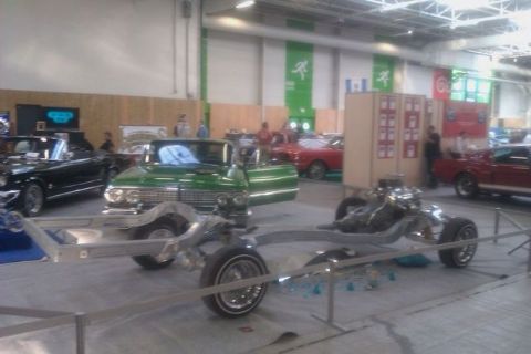 1991 Ford LTD Crown Victoria - A custom lowrider chassis is displayed in front of several classic cars at an indoor event.