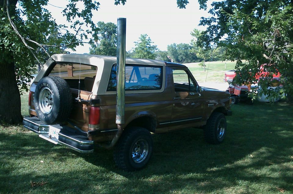 1987 Ford Bronco with a tall exhaust pipe and spare tire on the back, parked on grass