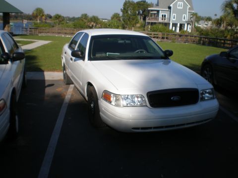 2004 Ford Crown Victoria - A white 2004 Ford Crown Victoria is parked in a lot, showing its front grille and headlights.
