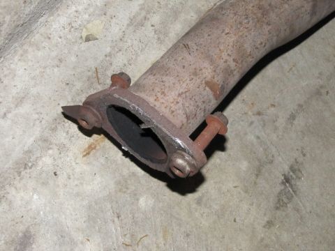 1995 Ford Bronco - Close-up of a rusty exhaust pipe flange, showing the connection point with two bolts and a gasket. The part is resting on a concrete surfac…
