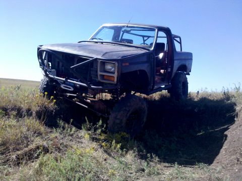 1986 Ford Bronco - This heavily modified SUV, likely from the early 1980s, is shown off-road with a prominent roll cage and custom bumper.