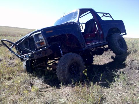 1986 Ford Bronco - Modified Ford Bronco with off-road tires and a custom bumper navigates rough terrain.
