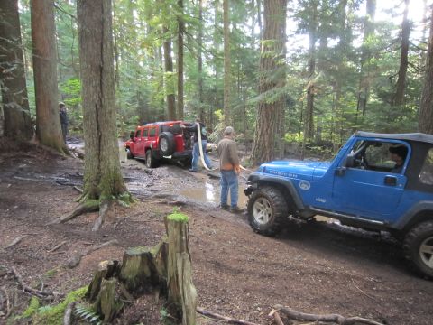 2008 Jeep Wrangler - Two off-road vehicles, a blue Jeep Wrangler and a red Hummer, navigate a muddy trail in a forest.