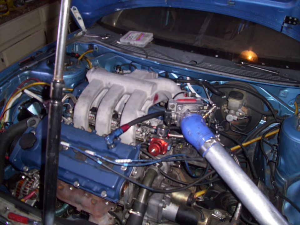 engine bay with blue valve cover, silver intake manifold, and large silver pipe connected to a blue turbo inlet