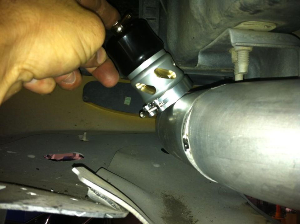 Hand holding a blow-off valve connected to a large pipe, likely part of a vehicle's exhaust or intake system