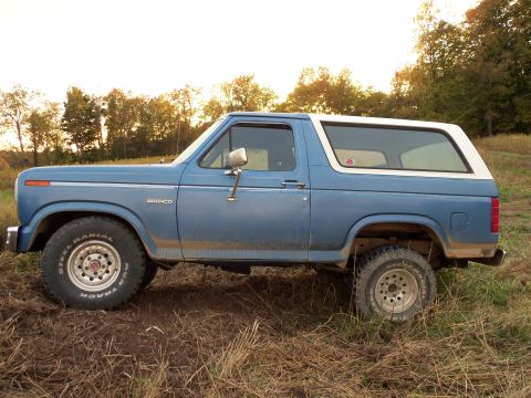 1985 Ford Bronco - This 1985 Ford Bronco, seen from the side, is parked in a field with trees in the background.