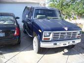 1985 Ford Bronco - A blue 1985 Ford Bronco with a camper shell parked in a driveway next to another vehicle.