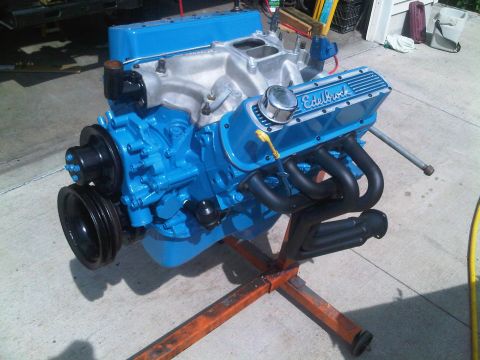1985 Ford Bronco - A blue engine with Edelbrock valve covers is displayed on a stand, with exhaust headers and a pulley visible.