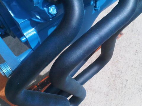 1985 Ford Bronco - Close-up view of a blue engine block and black exhaust manifold pipes, with a Supermotors.net watermark.