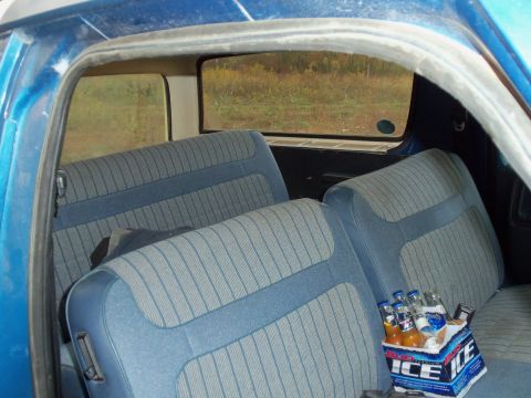 1985 Ford Bronco - The rear seats of a blue SUV are visible, with a six-pack of drinks on the seat.