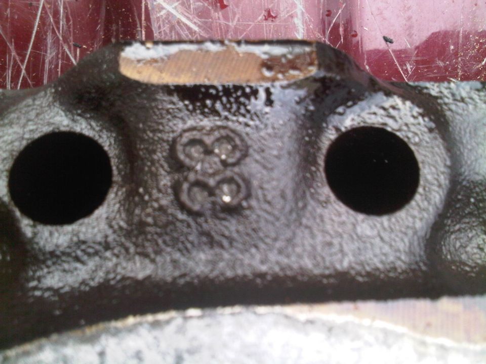 Close-up of a cast iron engine part showing the number 38 cast into it. Two bolt holes are visible