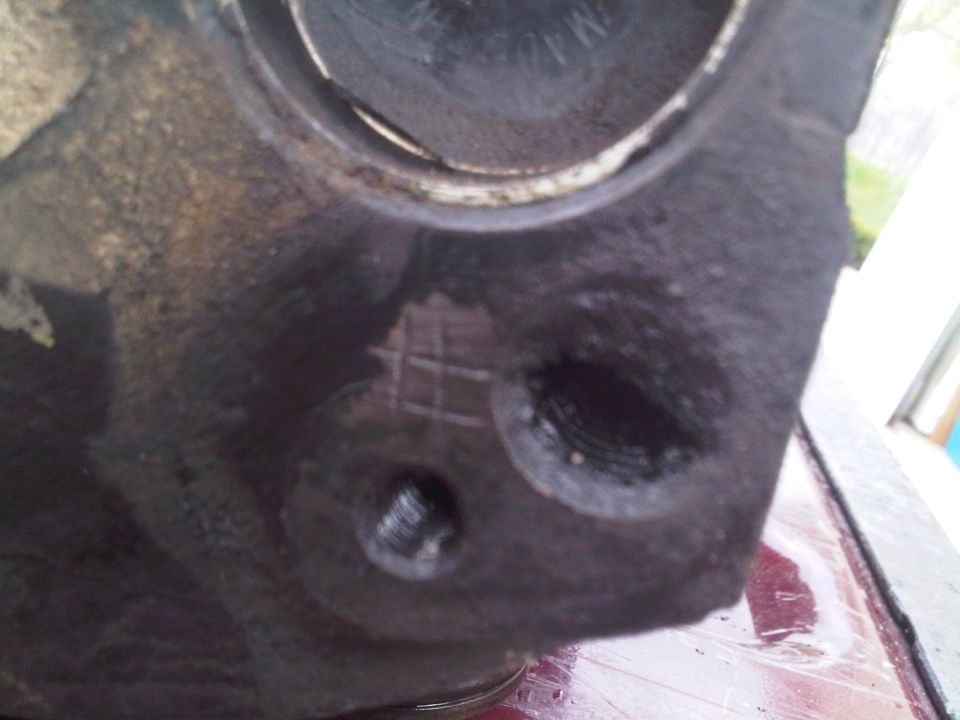 Close-up of black cast engine part showing two threaded bolt holes and a large machined bore