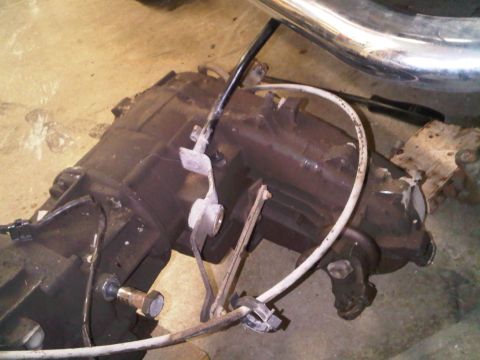 1985 Ford Bronco - Transmission assembly with various cables and linkages attached, resting on a concrete floor.