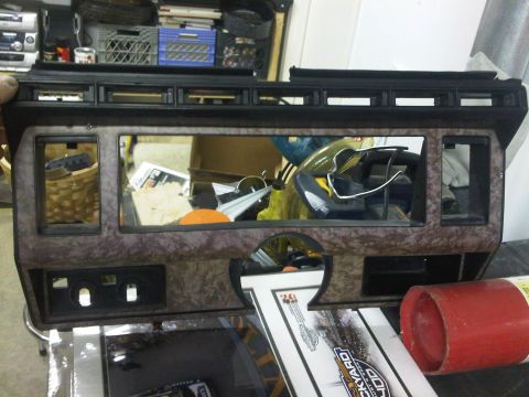 1985 Ford Bronco - Dashboard panel with faux wood grain trim and openings for electronics.