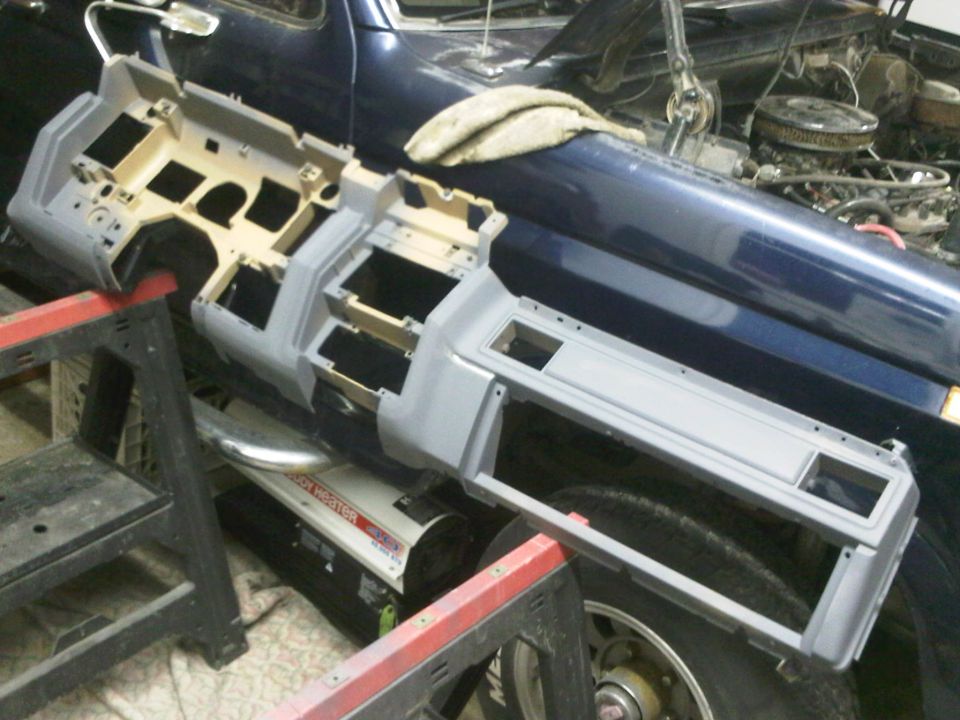 Gray dashboard assembly on sawhorses, with a blue vehicle interior and engine visible behind it