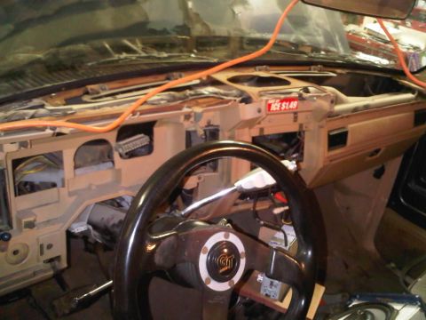 1985 Ford Bronco - The interior of a vehicle shows a disassembled dashboard with exposed wiring and an orange cable.