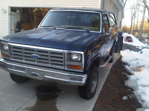 1985 Ford Bronco - Front view of a dark blue 1985 Ford Bronco parked outside a garage.
